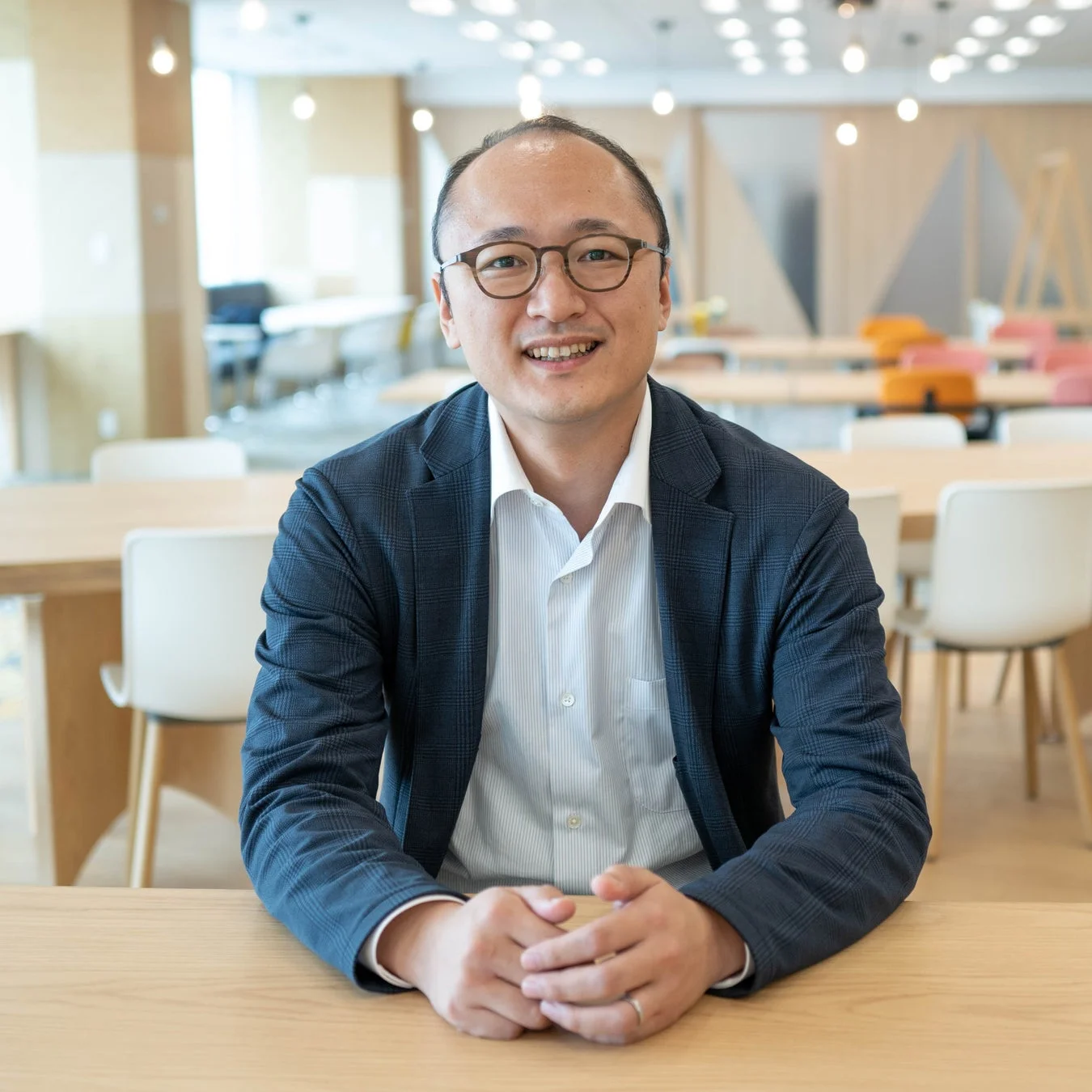 眼鏡をかけたアジア人男性がカメラに向かって笑顔で座っている。