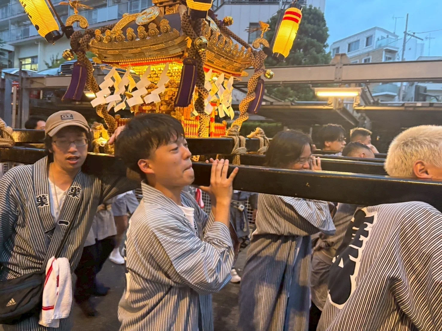 夜の街中で、法被を着た男性たちが豪華な装飾が施された神輿を担いでいる様子