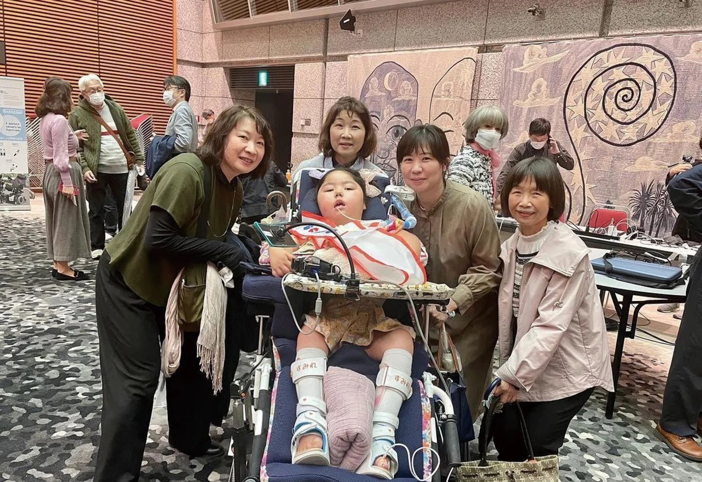車椅子に乗った子供を囲んで笑顔で写る集合写真
