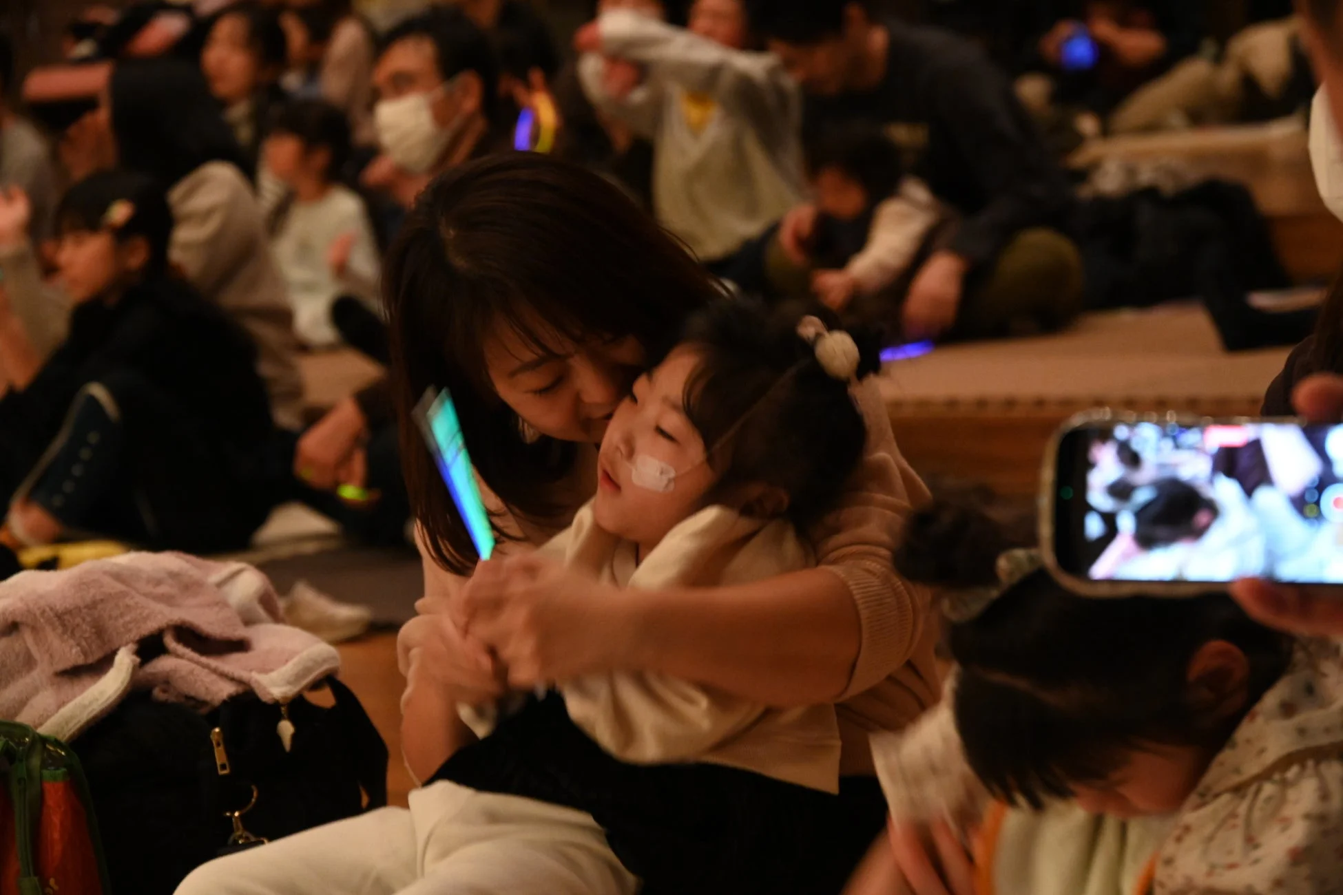 多くの人々が集まるイベント会場で、一人の女性が子供を優しく抱きしめている様子です。