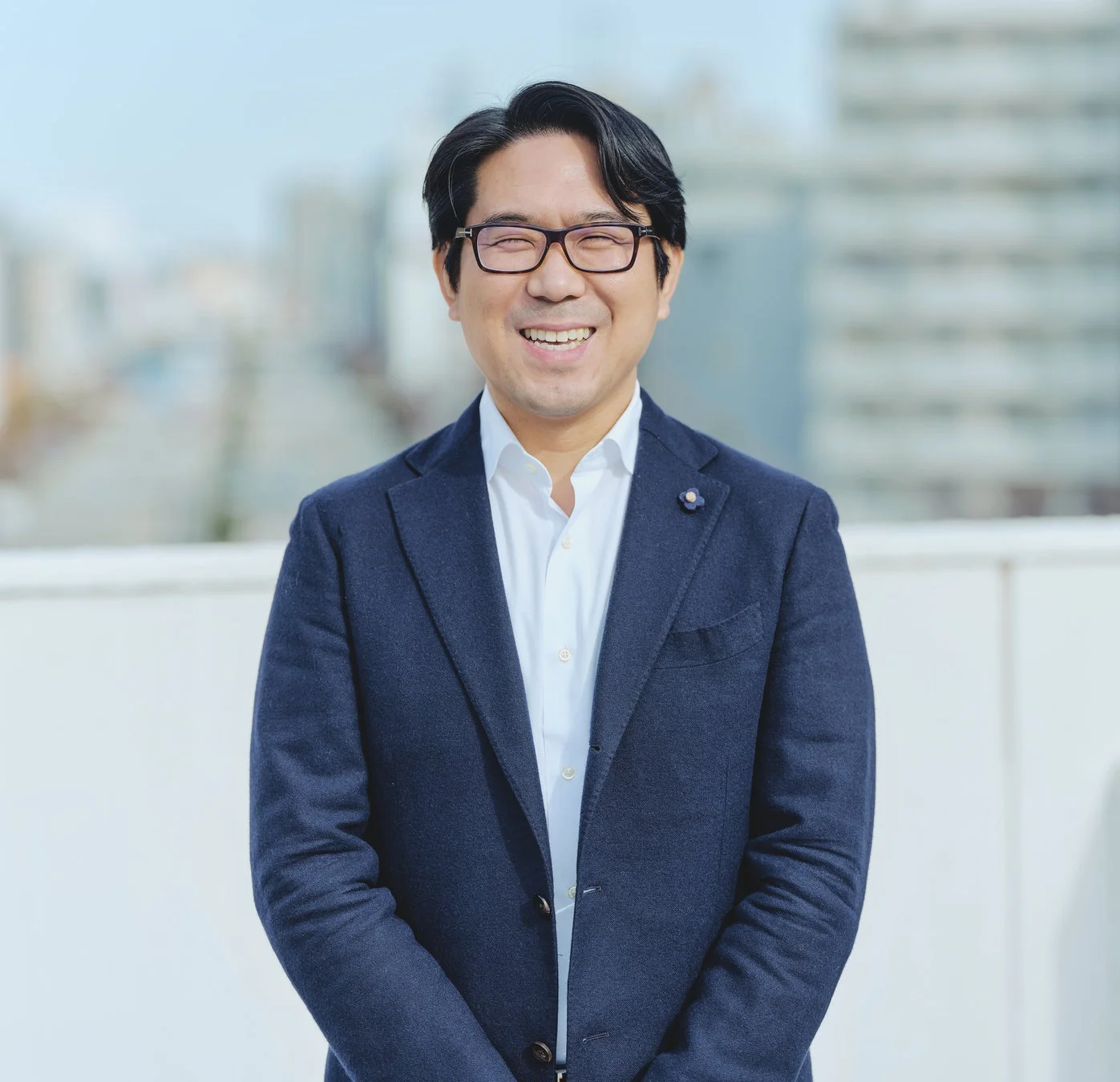 屋外で明るく笑顔を見せる眼鏡をかけたアジア人男性のビジネスポートレート。