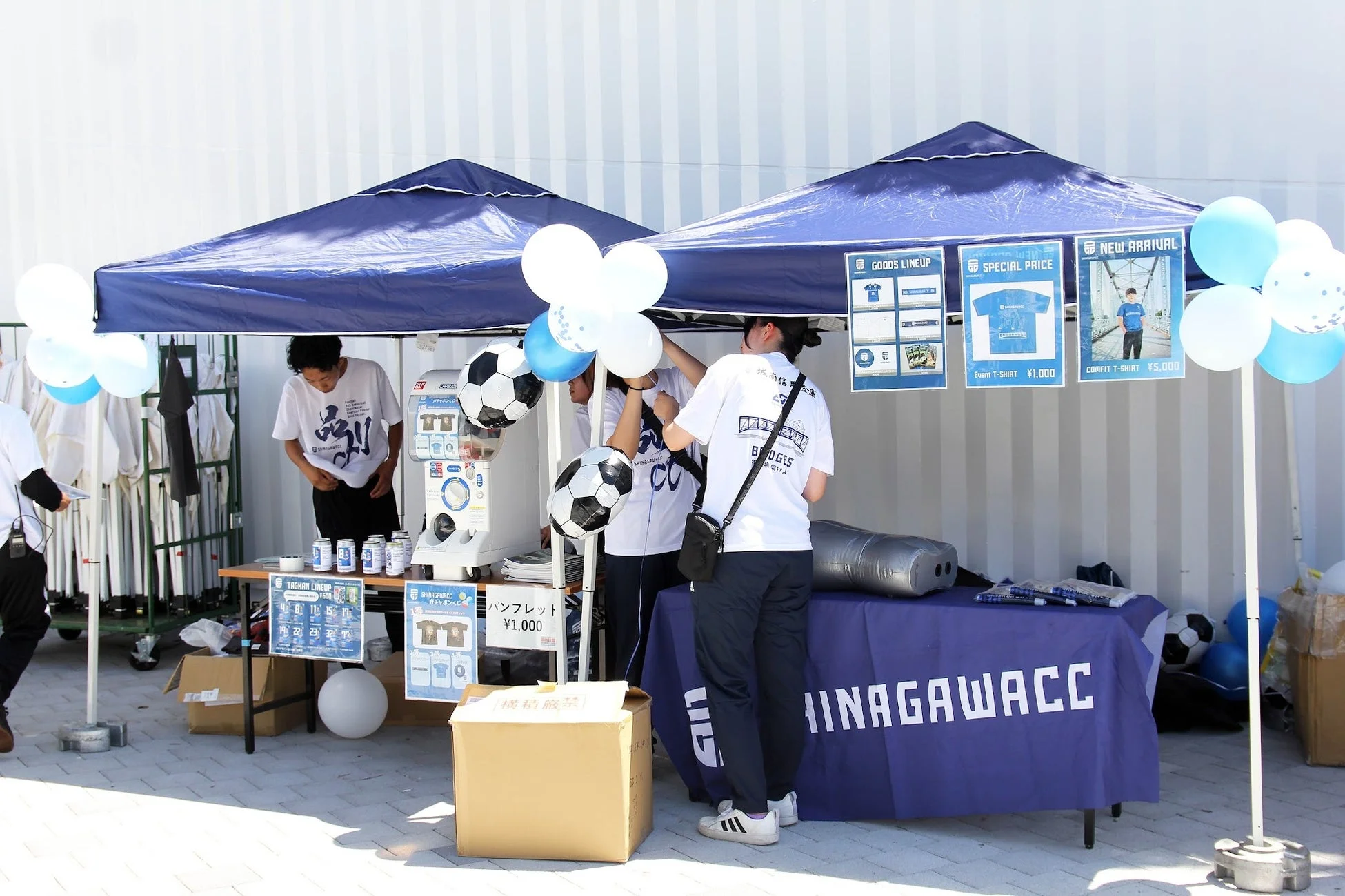 晴れた屋外で、青いテントの下に設置されたサッカークラブの物販ブース
