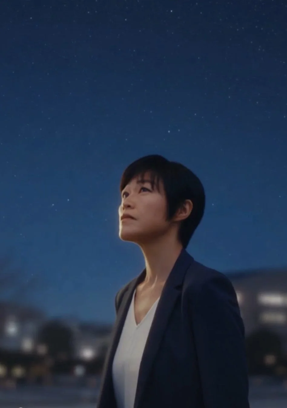 夜空を見上げるショートヘアの女性のポートレート。澄んだ暗い空には多数の星が輝き、女性は何かを思案するように遠くを見つめています。