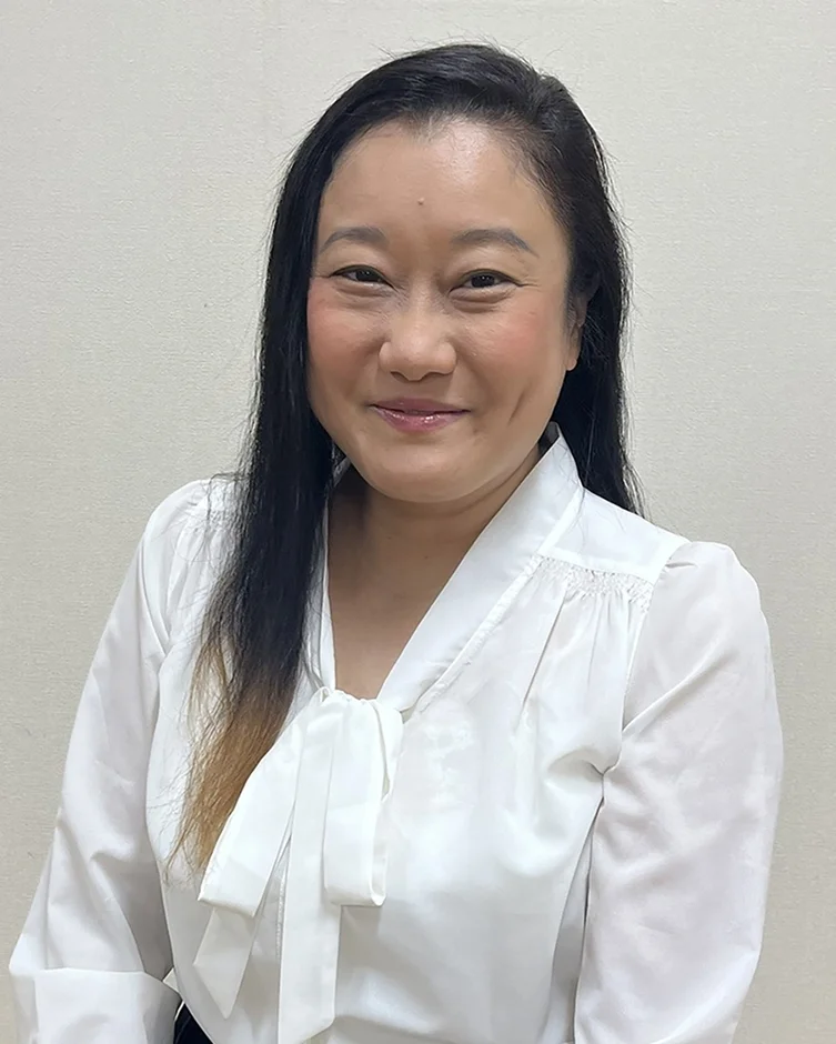 白いボウタイブラウスを着用したアジア人女性のポートレート写真です。女性はカメラに向かって穏やかな笑顔を見せており、親しみやすい印象を与えます。