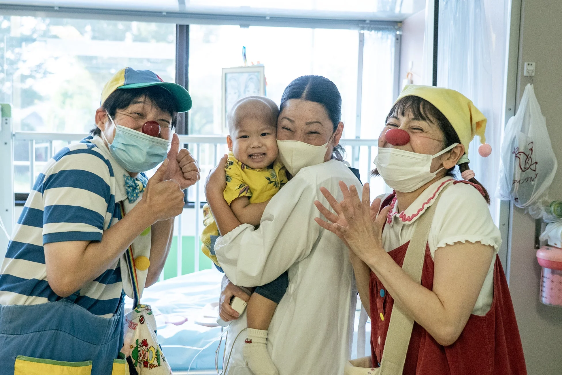 病室で赤ちゃんを抱く大人と交流するクリニクラウン