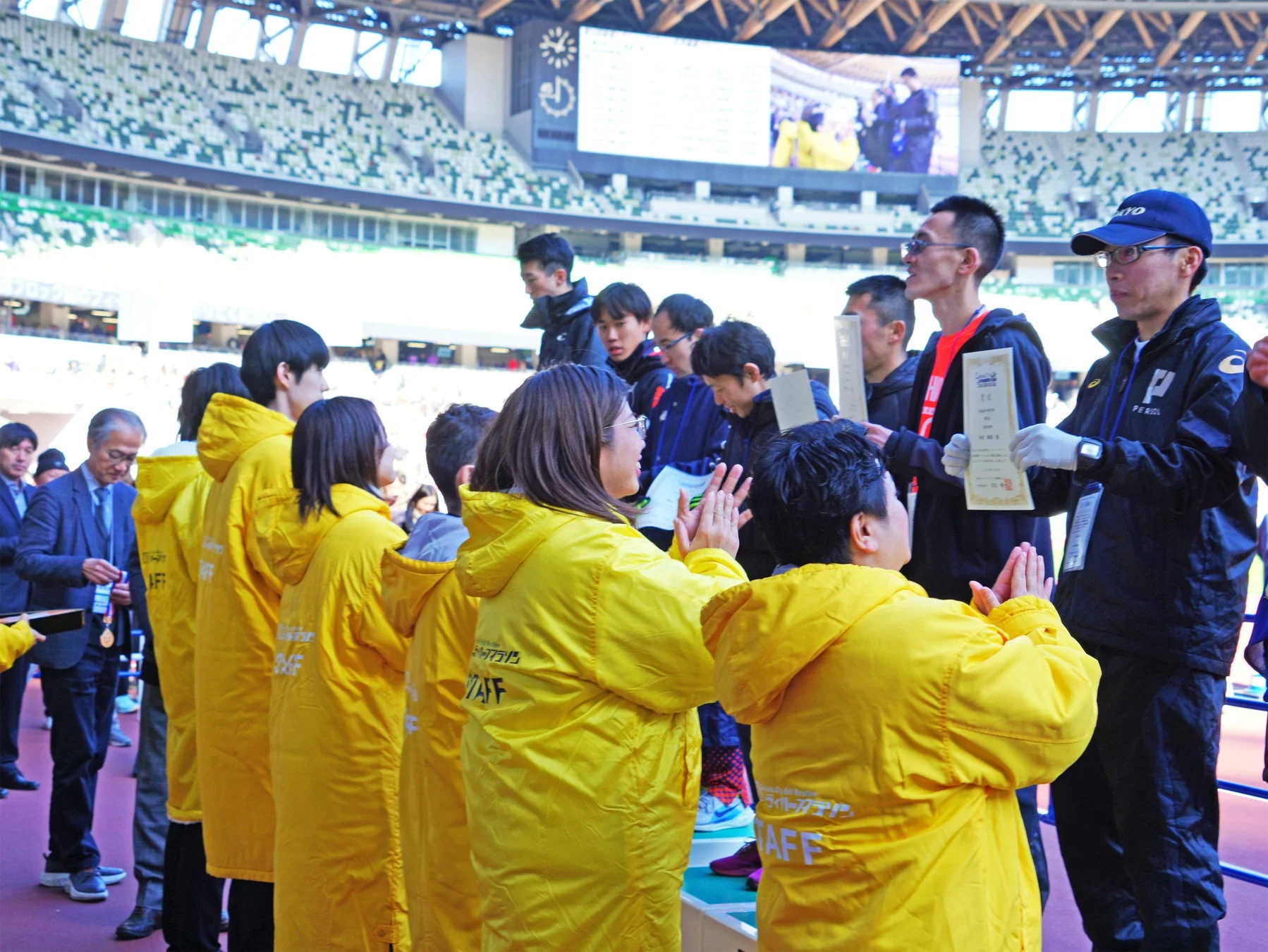スタジアムでスタッフが集まり、証明書が授与されている様子