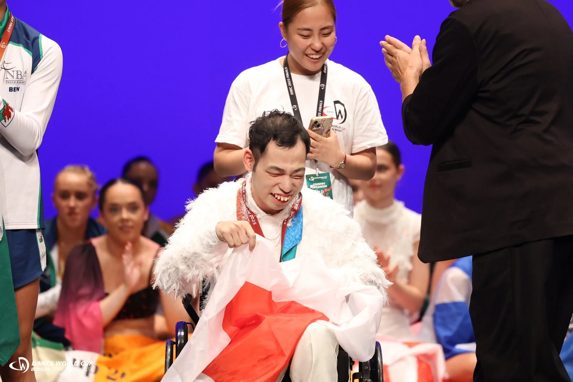 車椅子に乗った男性が日本の旗とメダルを手に満面の笑みを浮かべている様子