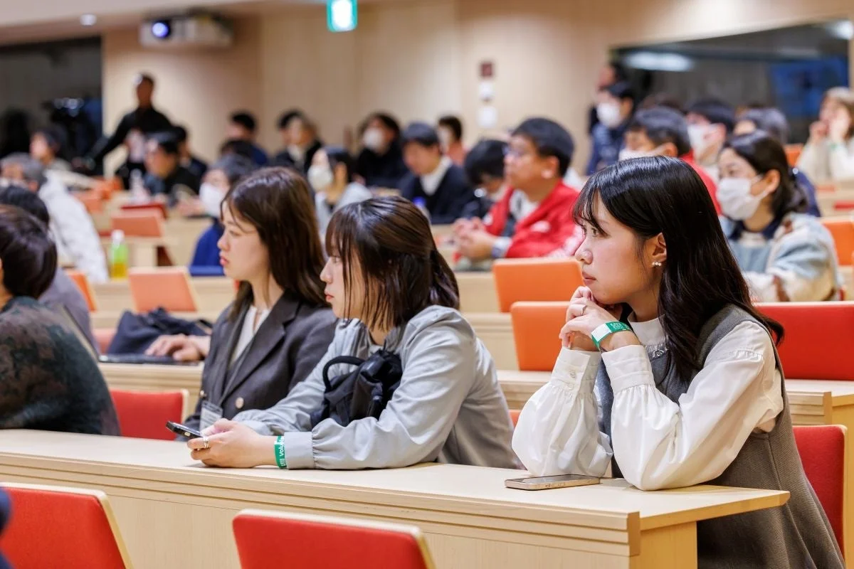 講義室やセミナー会場で、多くの若者たちがプレゼンテーションに集中して耳を傾けている様子