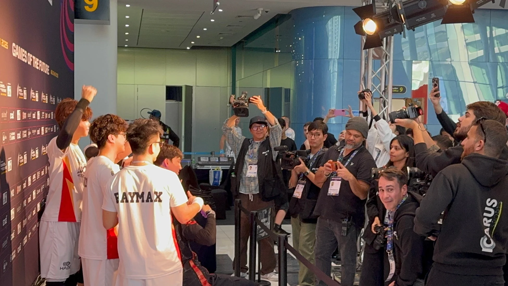 eスポーツイベントで、選手たちが多数のメディアに囲まれ、写真撮影や取材を受けている様子