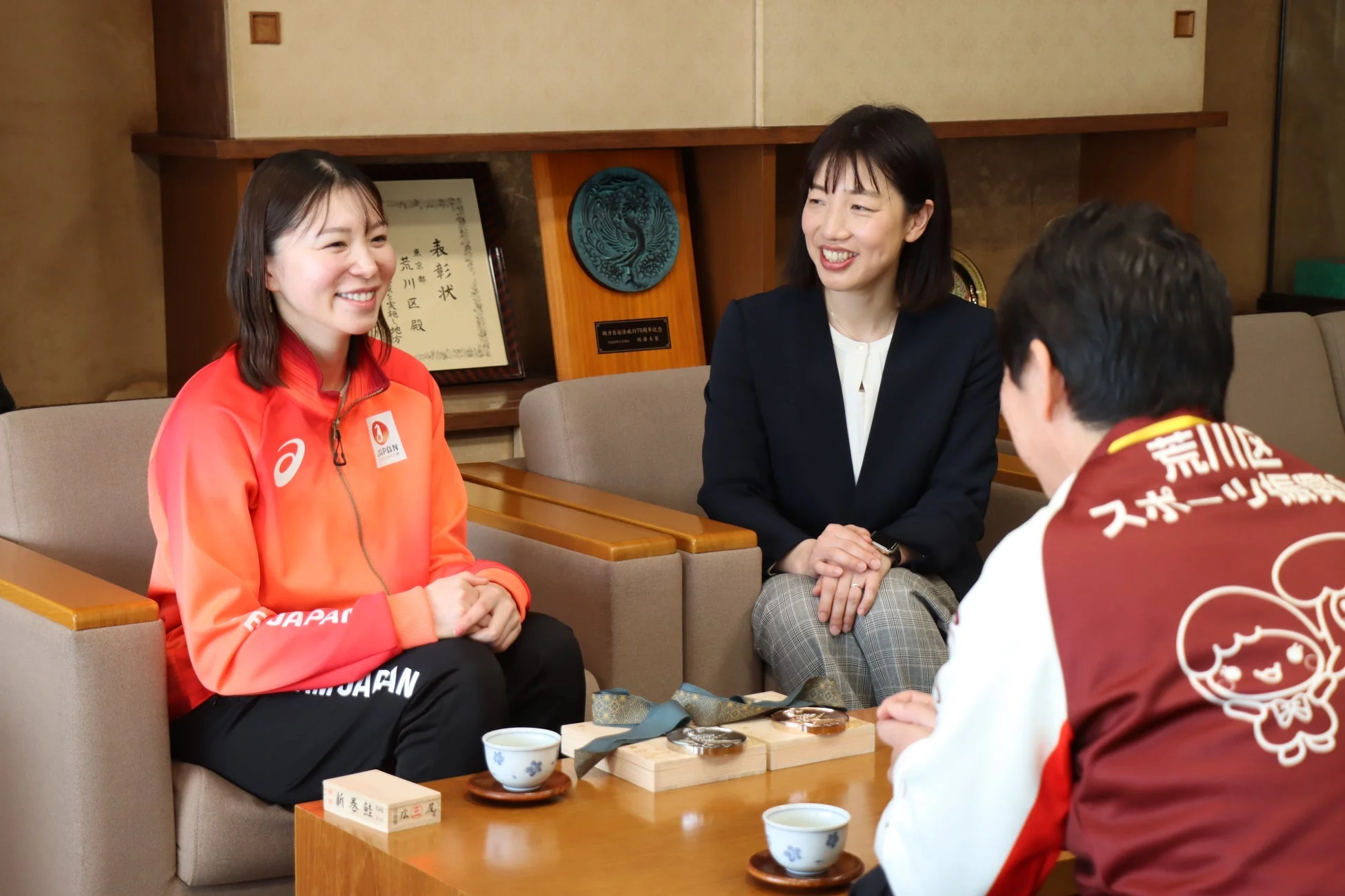 スポーツウェアを着た女性が、他の2人と和やかに談話している様子