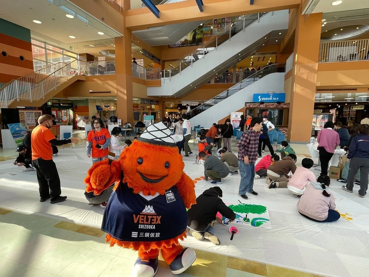 マスコットが見守る中、多くの人が絵を描く様子