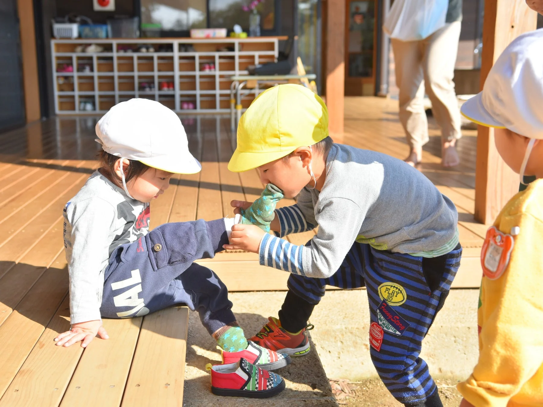 園児が別の園児の靴下を履かせるのを手伝っている画像