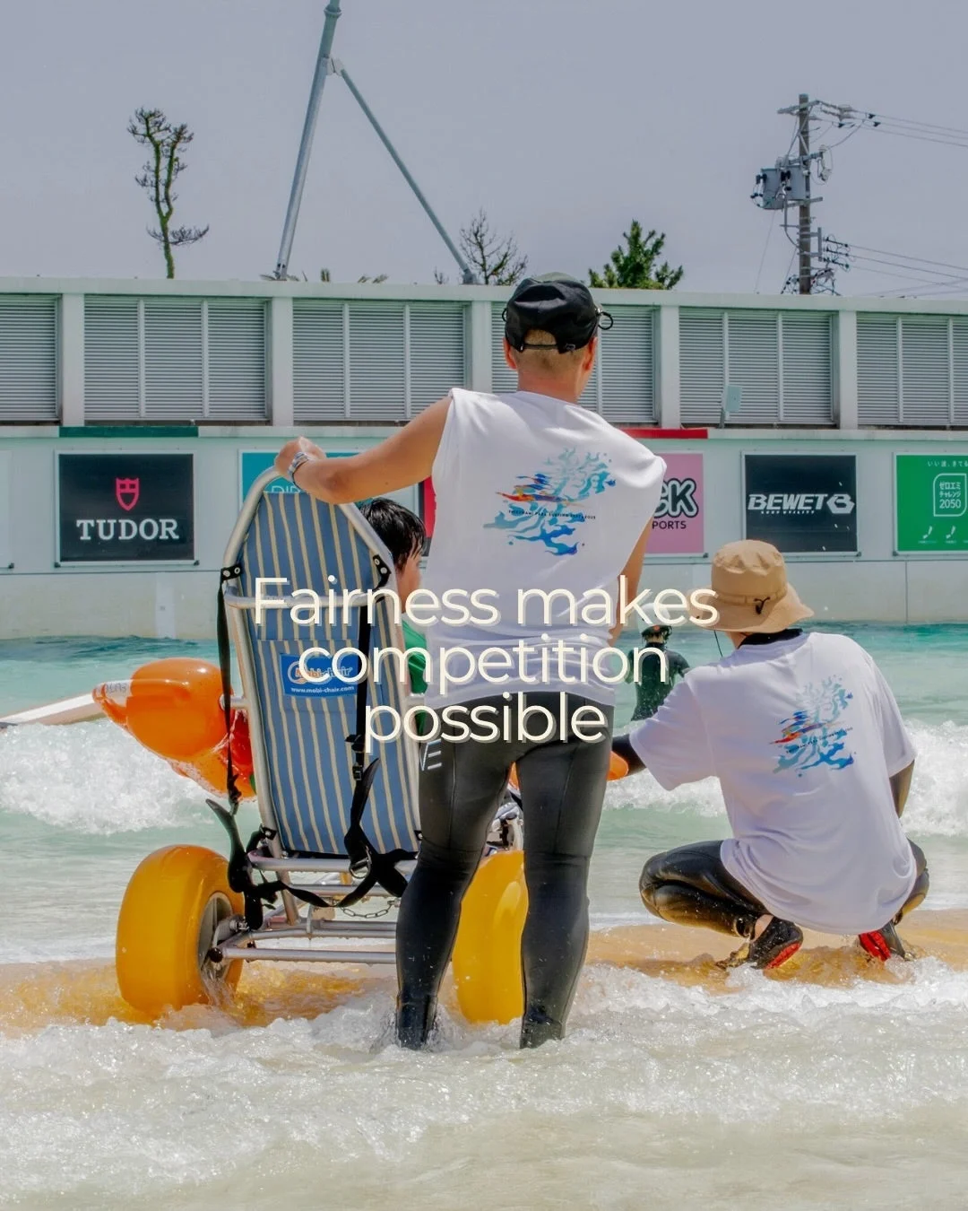 水陸両用車椅子で波打ち際にいる人々と「Fairness makes competition possible」のメッセージ
