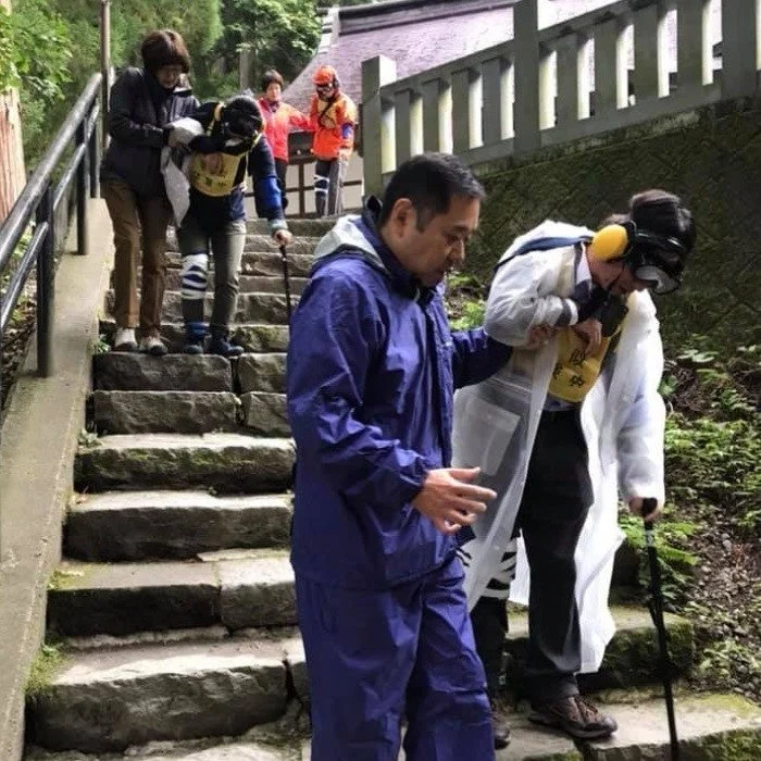 屋外の石段を介助されながら下りる人々