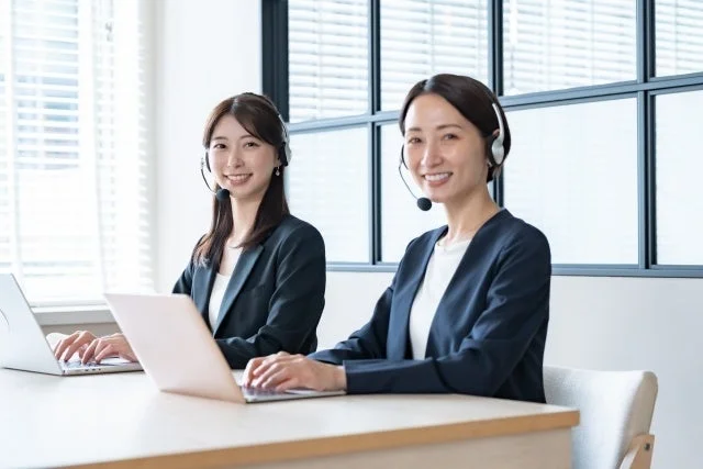 ヘッドセットを装着し、笑顔でパソコンを操作するコールセンターの女性