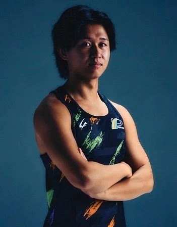 青緑色の背景を背に、腕を組んで立つ短髪のアジア人男性アスリートのポートレートです。