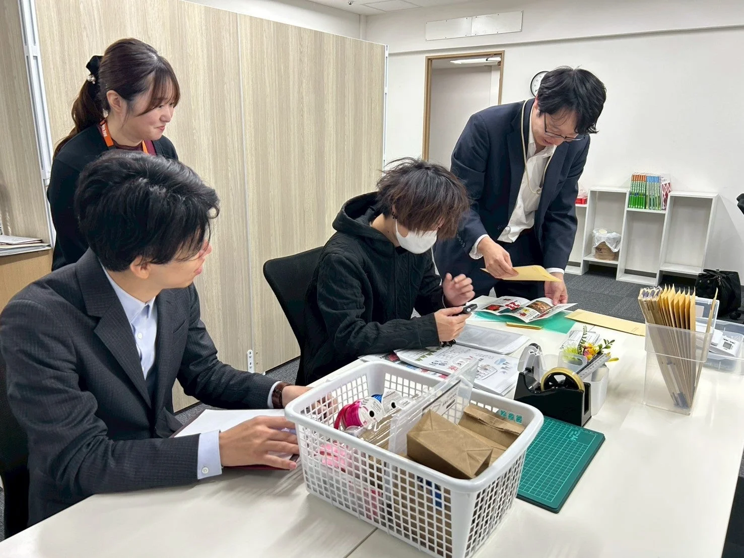 オフィスで4人がデスクを囲み、資料を見ながら打ち合わせ