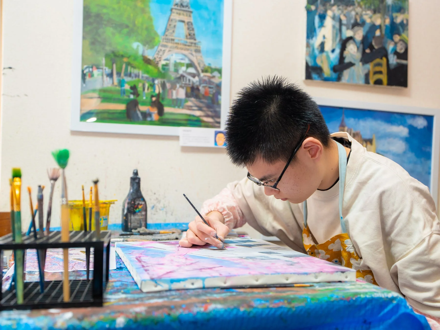 アトリエのような空間で、真剣な表情でキャンバスに絵を描く若い男性