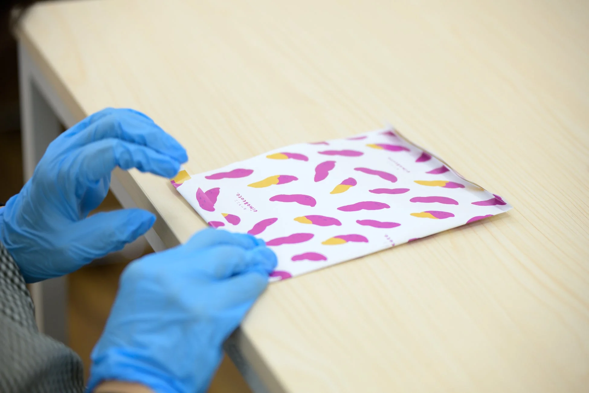 青い手袋をはめた手が、サツマイモのような模様が描かれた白いパッケージを扱っている