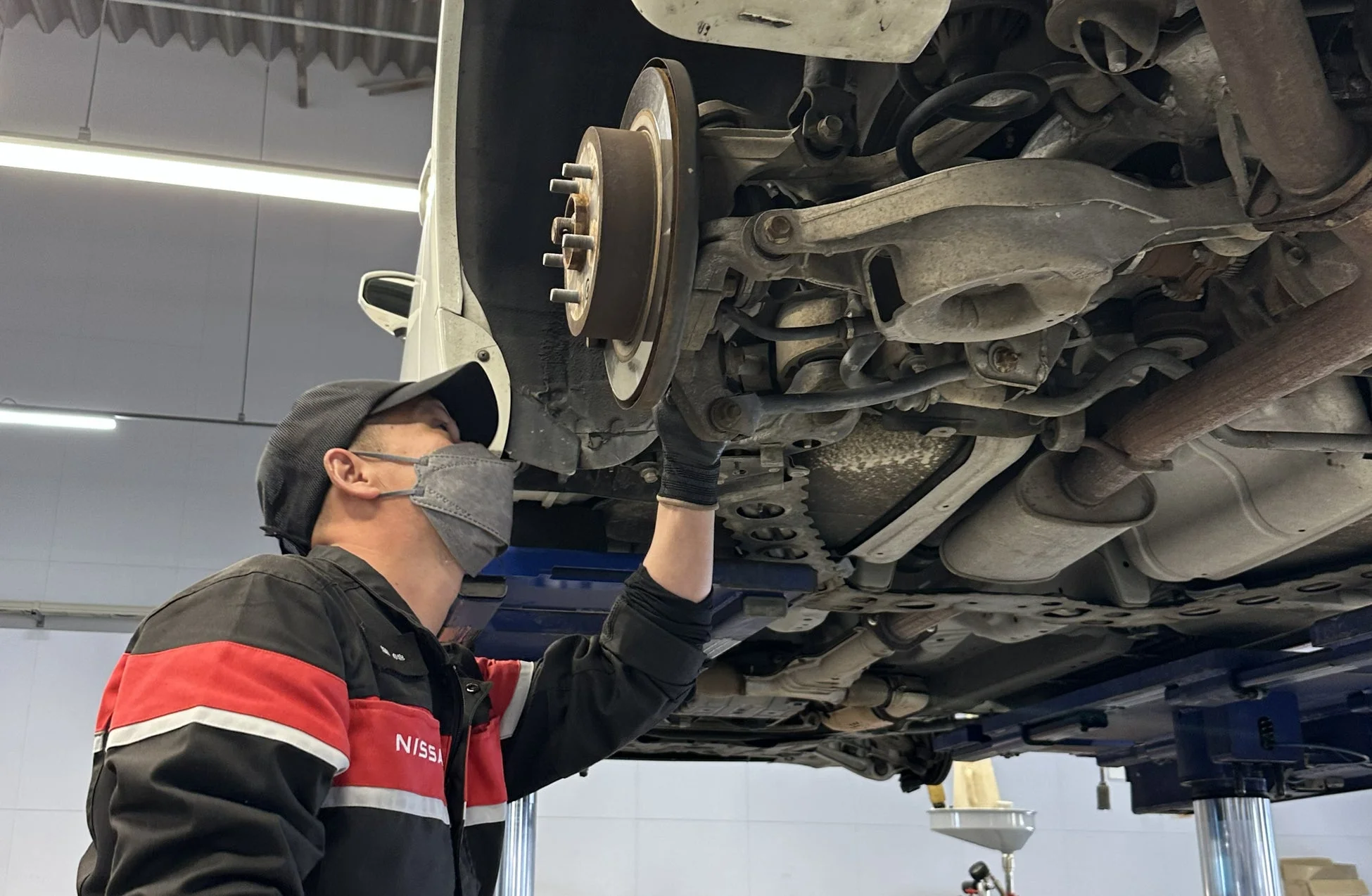 整備士がリフトアップされた車の足回りを点検している様子