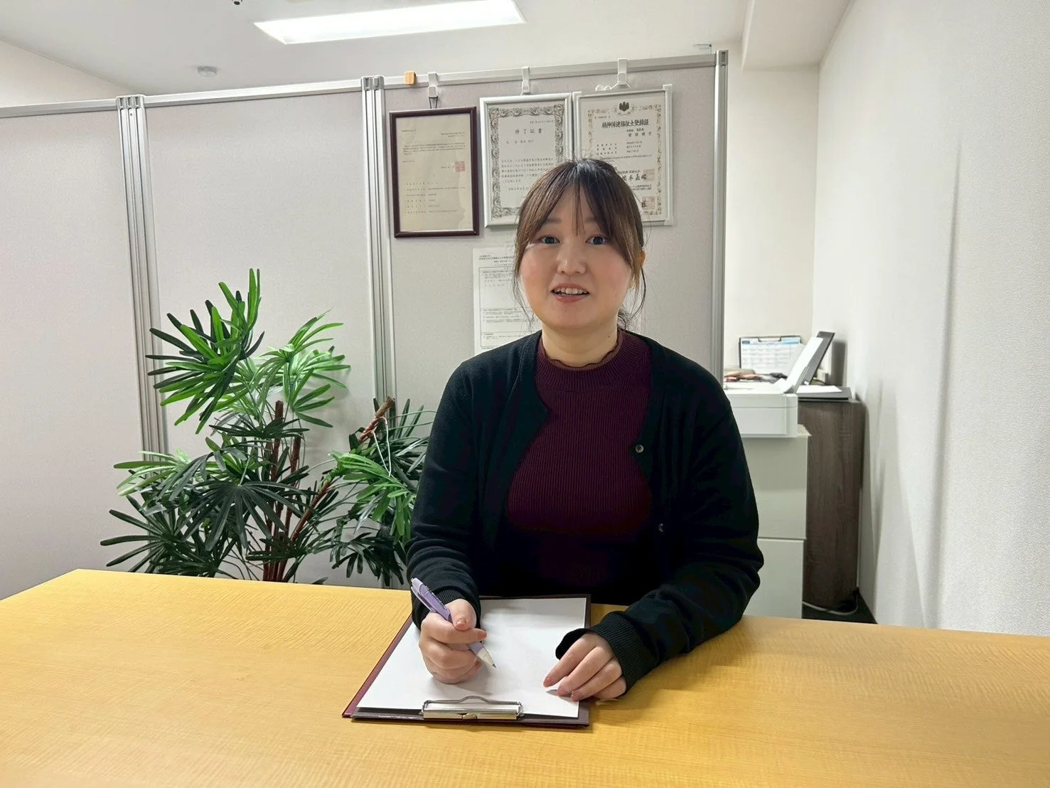 女性がデスクでペンを持ちカメラを見つめるポートレート