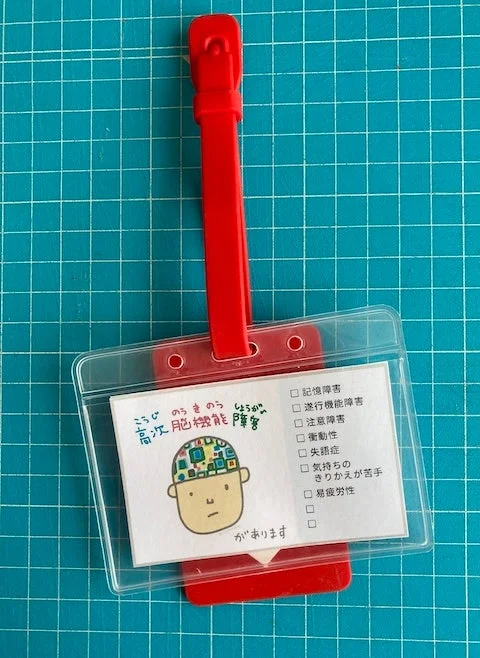 赤いストラップ付きのカードホルダーに、高次脳機能障害の症状がリストされた啓発カード
