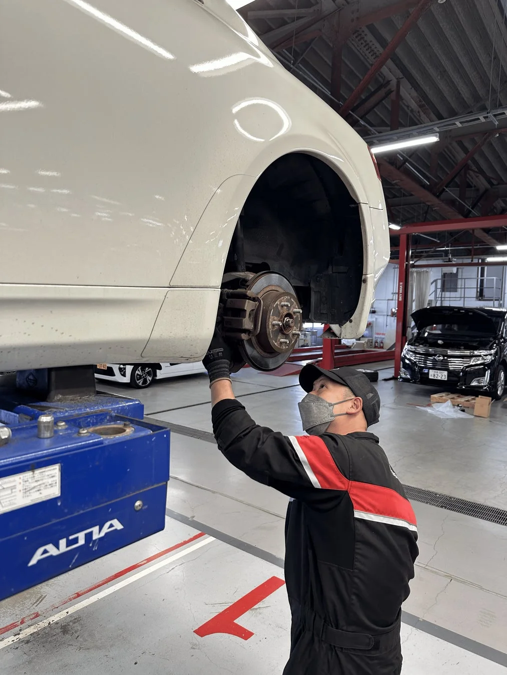 自動車整備工場で、メカニックがリフトアップされた車の後輪部分を点検・修理している様子