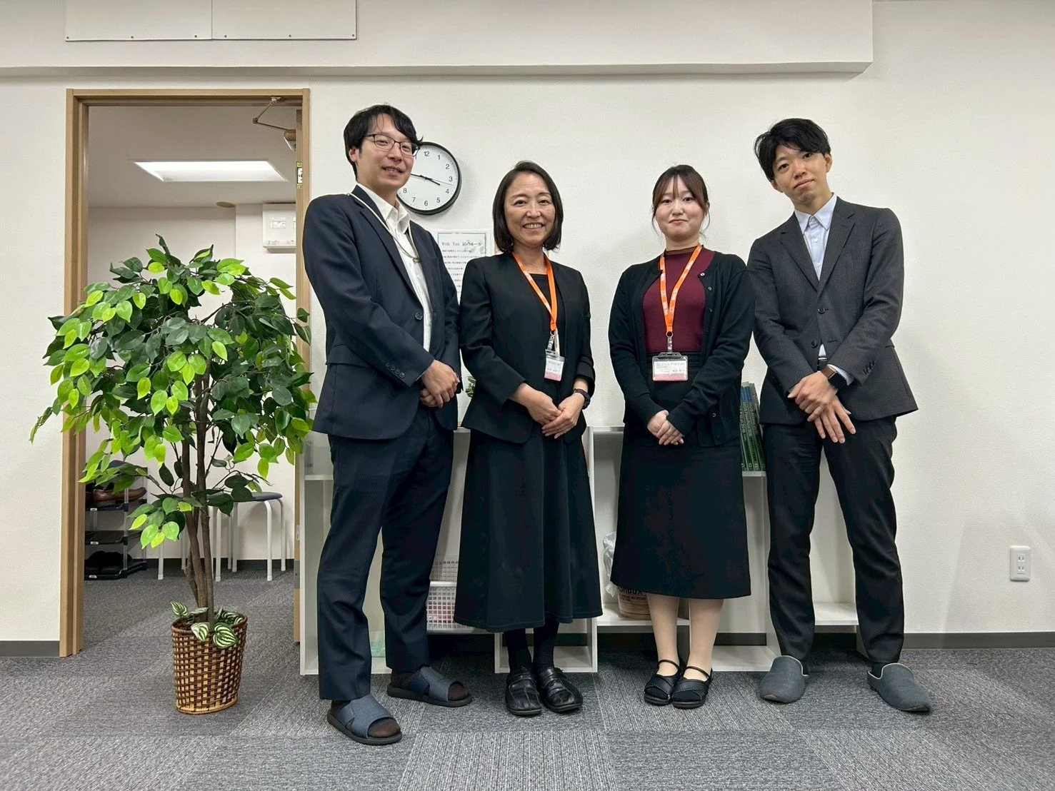 オフィスで4人が笑顔で立っている集合写真