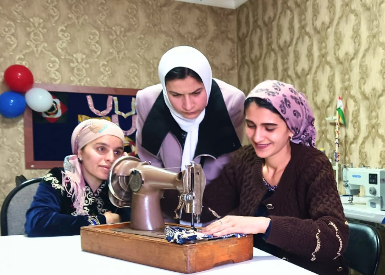 3人の女性がミシンの周りに集まり、裁縫作業に励んでいます