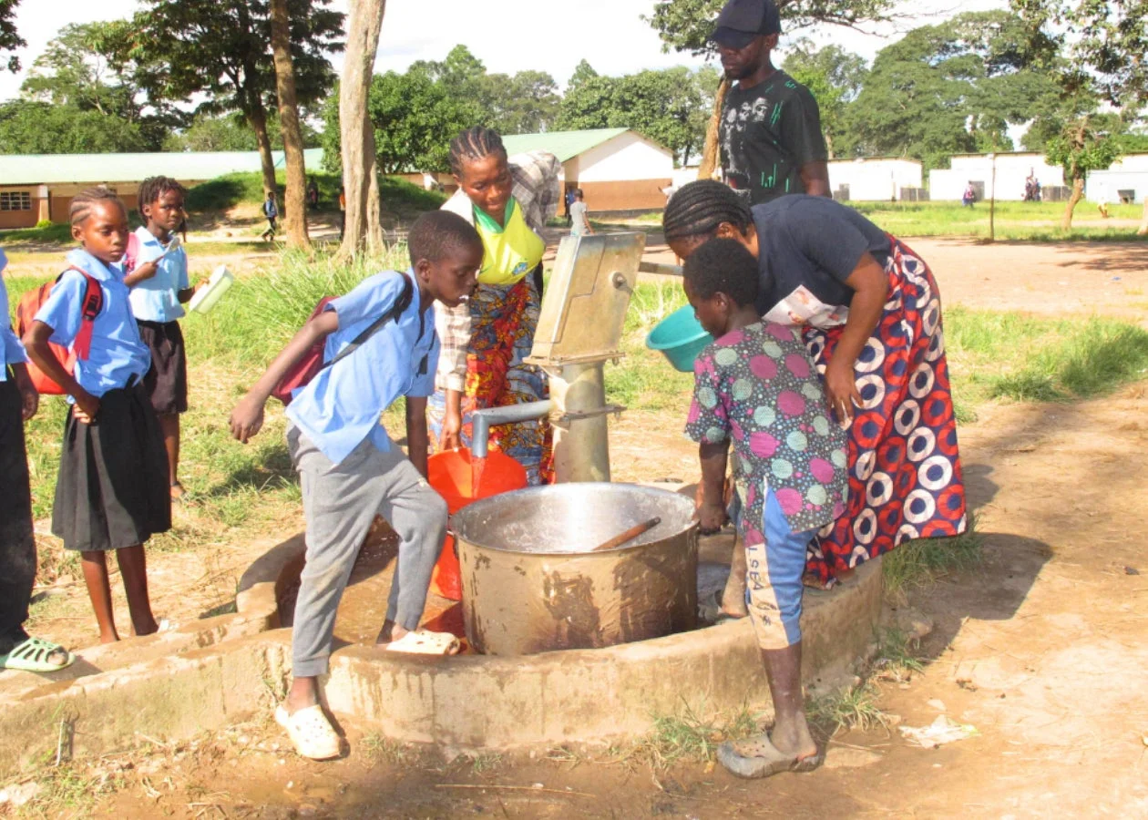 アフリカの屋外で、子供たちと大人が手動ポンプを使って水汲みをしている様子
