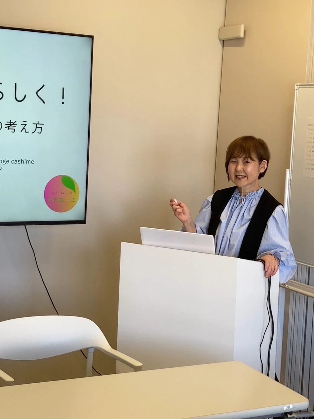 笑顔の女性がスクリーンと演台を前にプレゼンテーションを行っている様子
