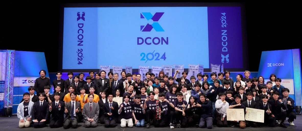 DCON 2024のイベント会場での集合写真。大勢の参加者や関係者が笑顔でポーズをとっている