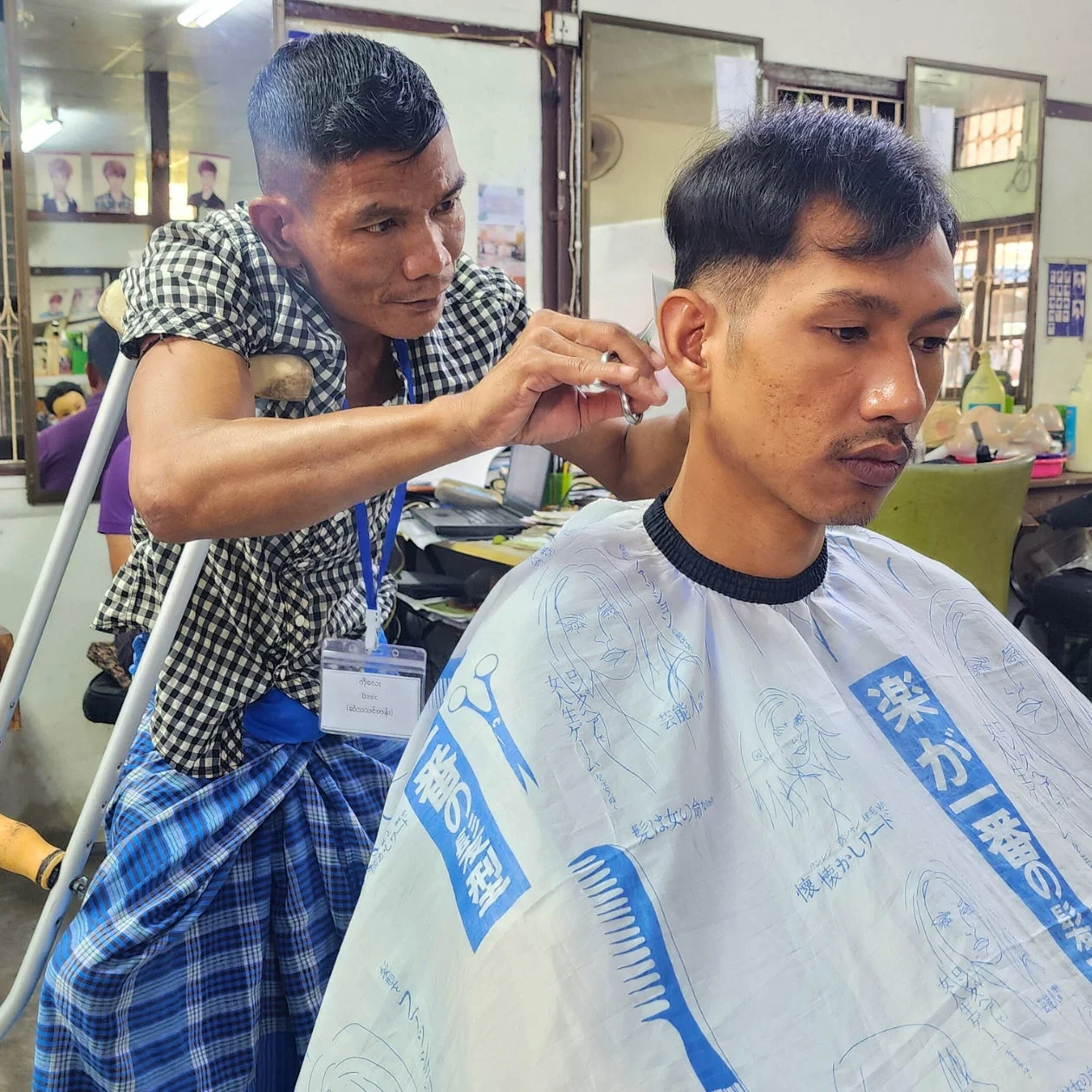 理髪店で、杖を使用しながらも客の髪を丁寧にカットする理容師の姿