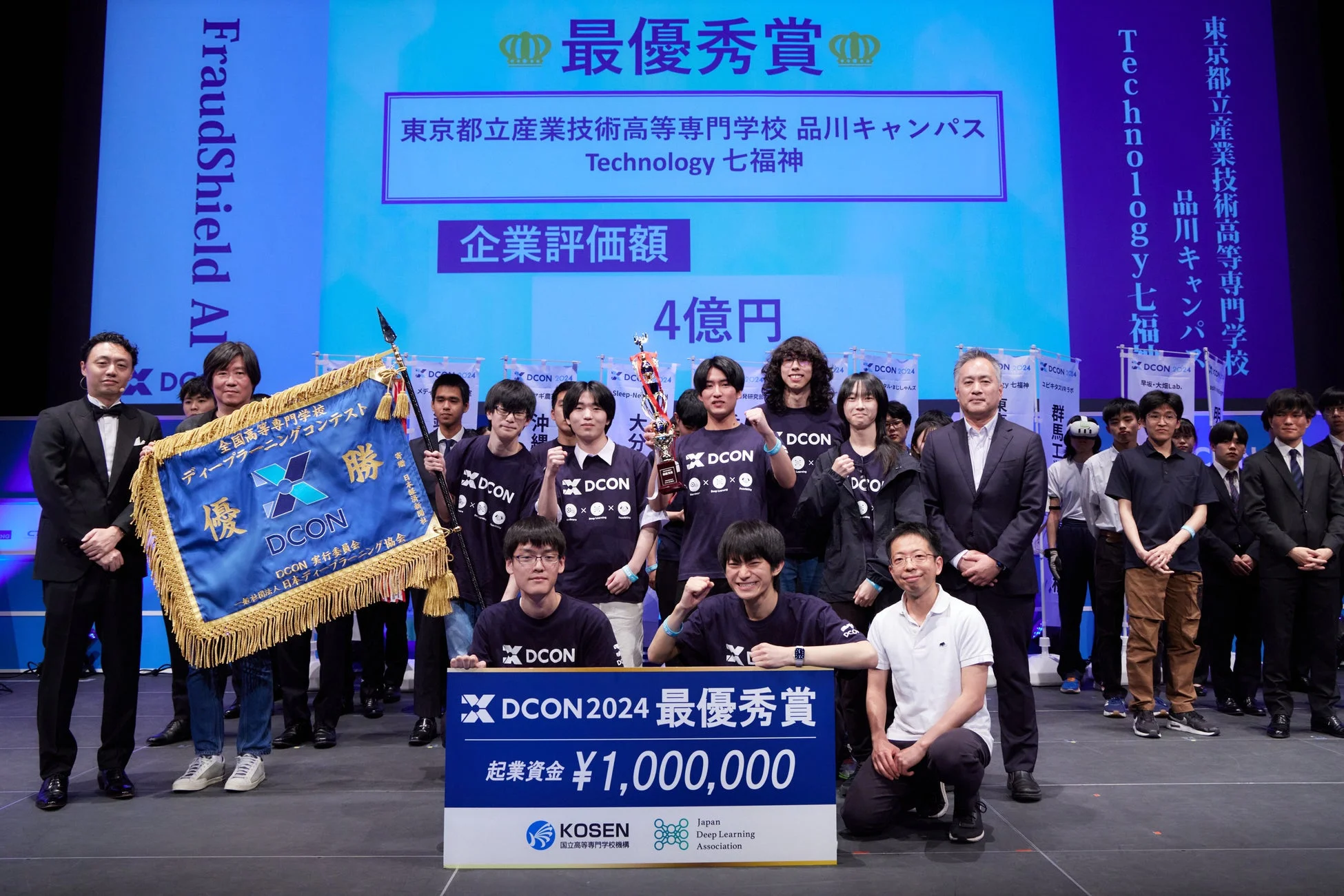 DCON 2024で最優秀賞を受賞し、優勝旗とトロフィーを手に喜ぶ「Technology 七福神」チームの集合写真
