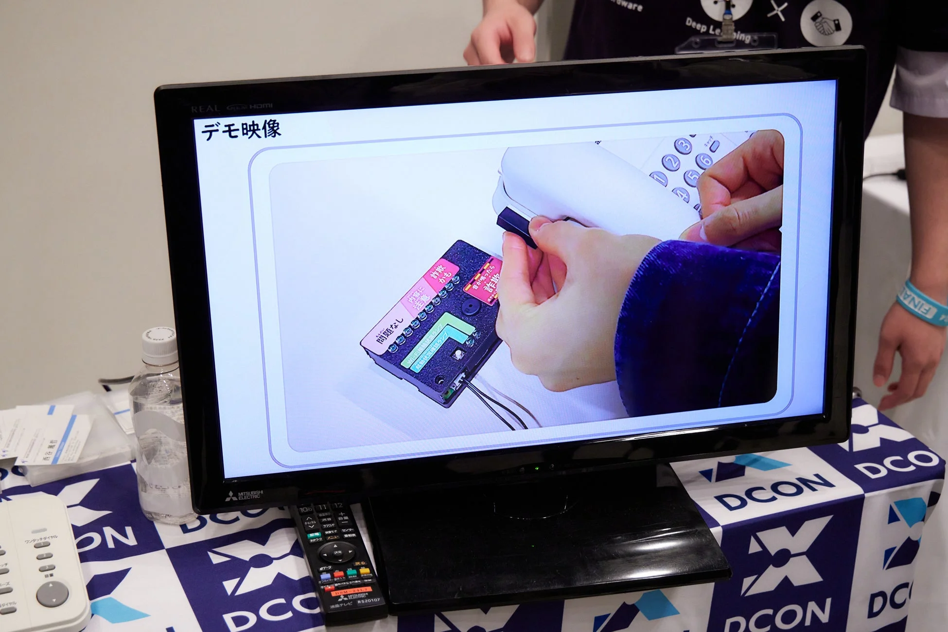 デモ映像を映し出すテレビと、手元の電子機器を操作する様子