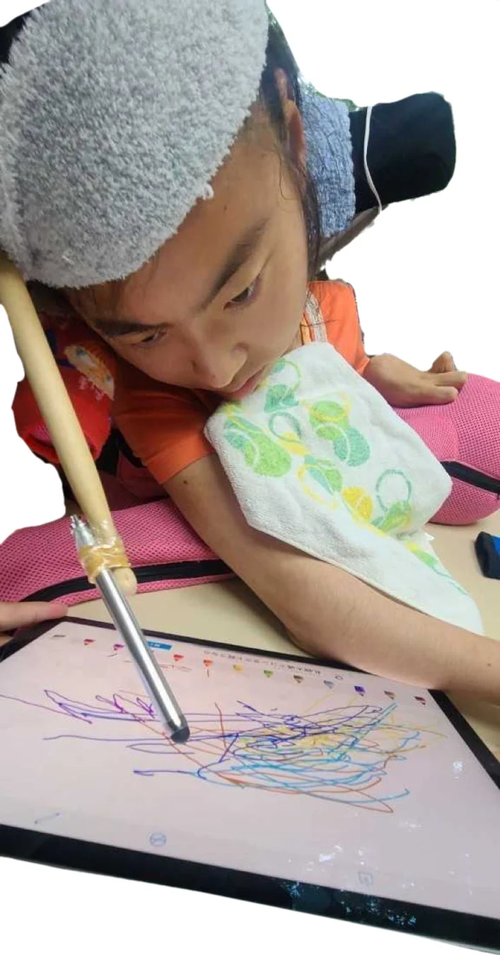 頭部を支えられたRIKOPINさんが、特製の長いペンを使ってタブレットで絵を描いている様子