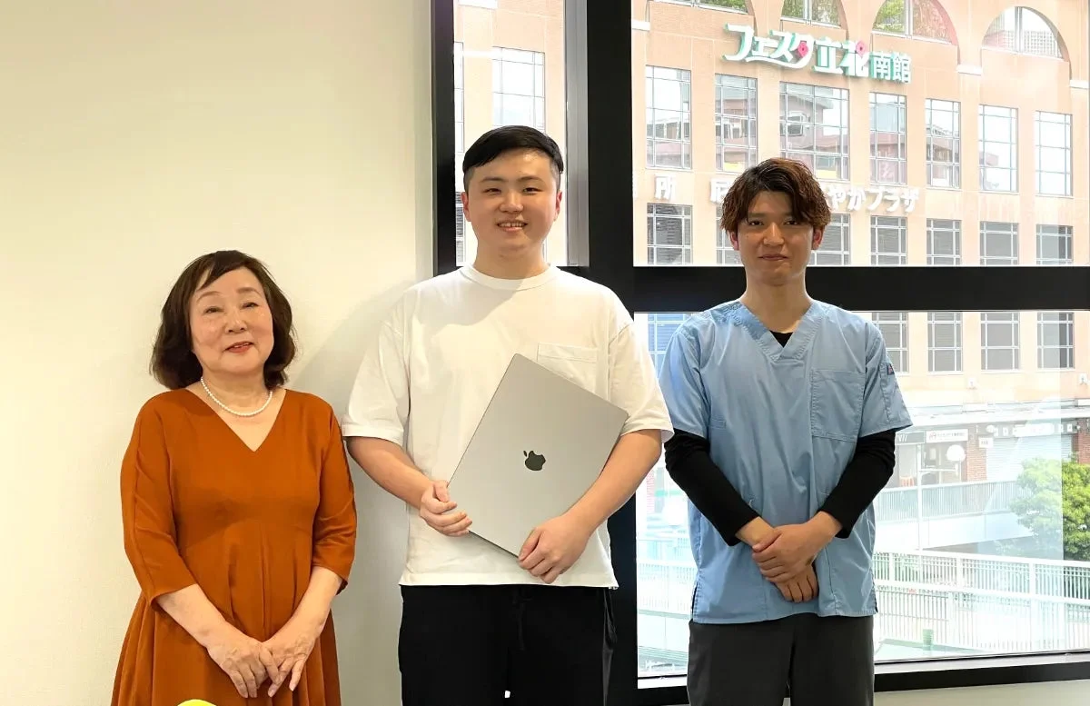 3人の人物が笑顔で並んで立っている集合写真です。
