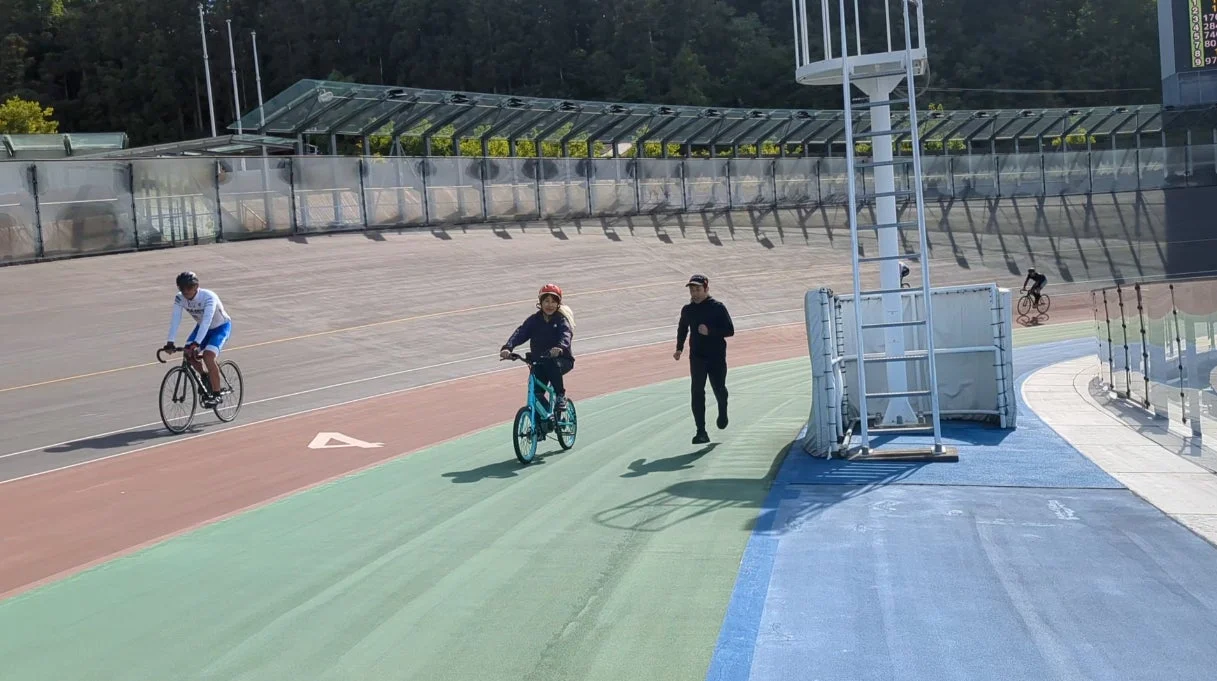 晴れた日に屋外のトラックでサイクリングとランニングを楽しむ人々が写っています