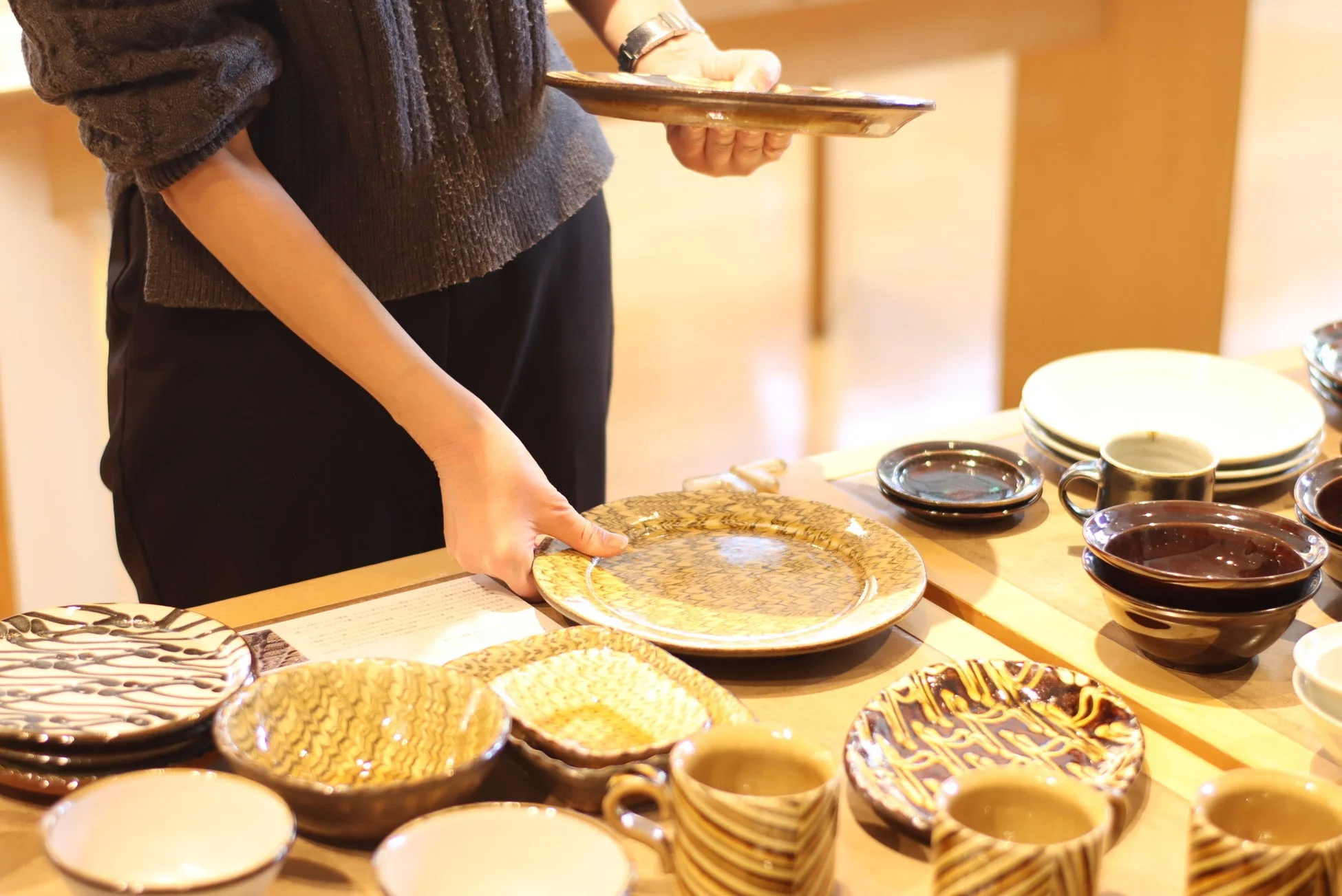 女性が様々なデザインの陶器や和食器の中からお皿を選んでいる様子です。