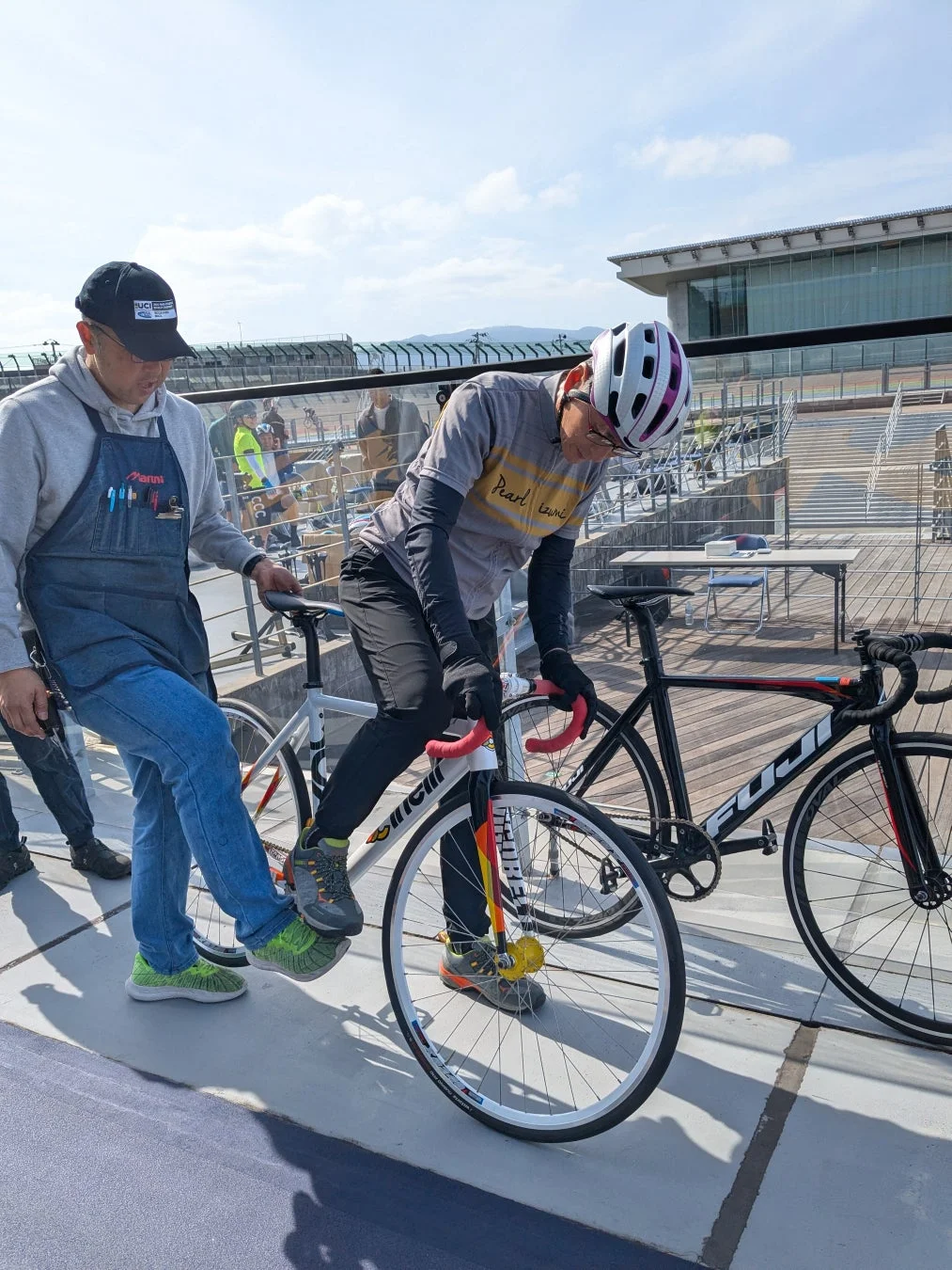 屋外の競技場で、2人の男性が自転車を準備している様子です