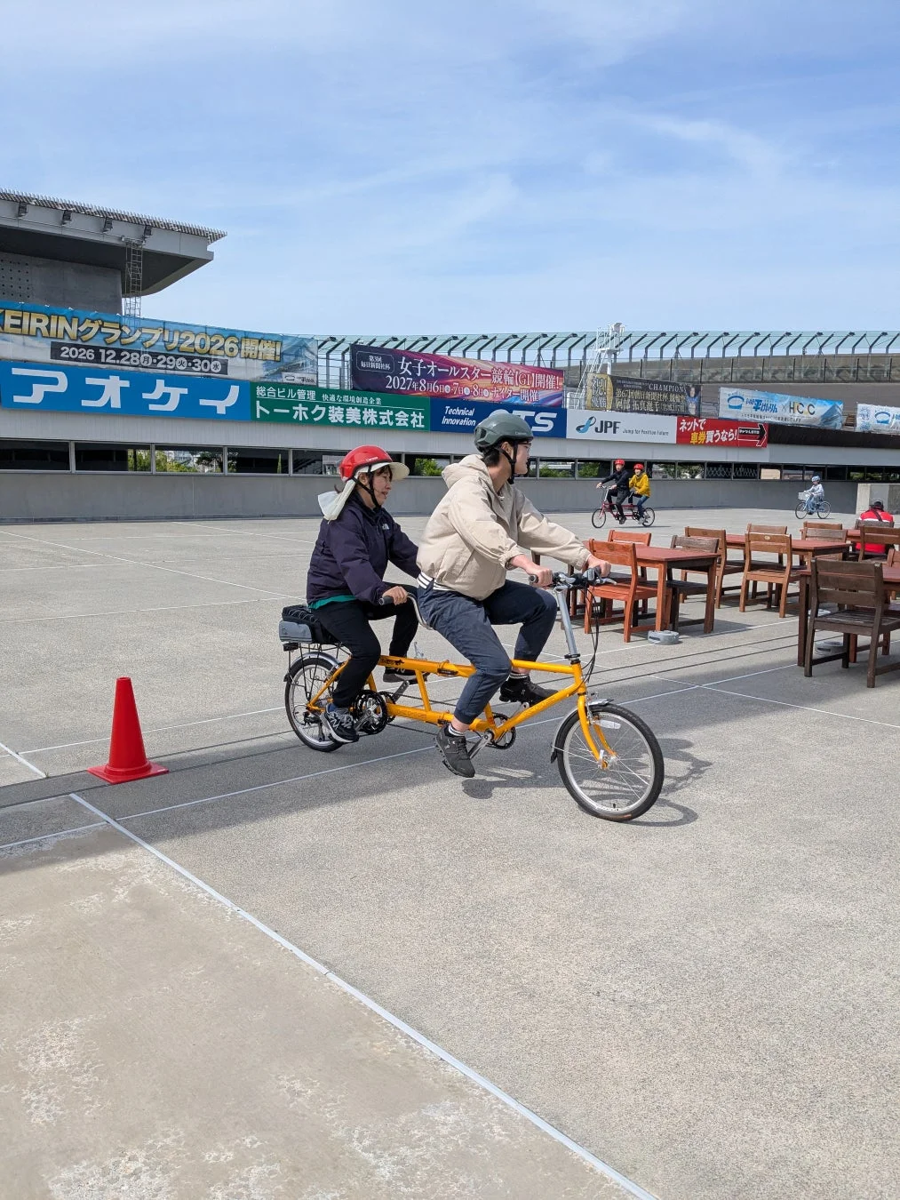 晴天の下、広々とした屋外で二人がタンデム自転車に乗っている様子が写っています