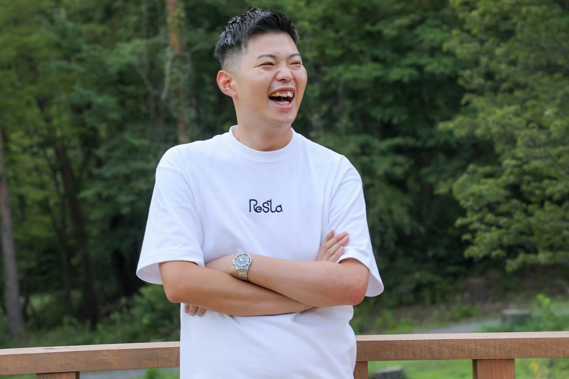 屋外で白いTシャツを着た若い男性(松川代表)が笑顔で写っているポートレート。