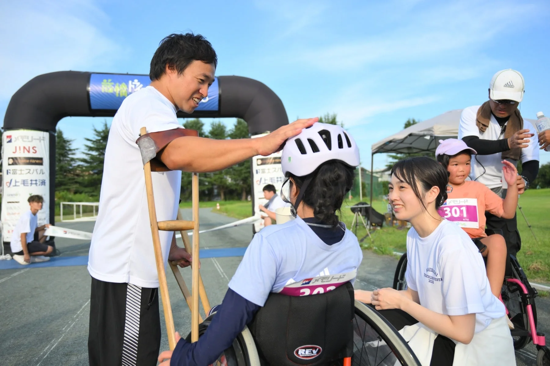 屋外のスポーツイベントで、義足の男性が車椅子の参加者に笑顔で優しく接している様子