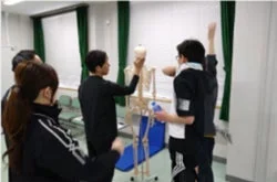 複数の人が人体模型の骨格標格を囲んで学習している様子。