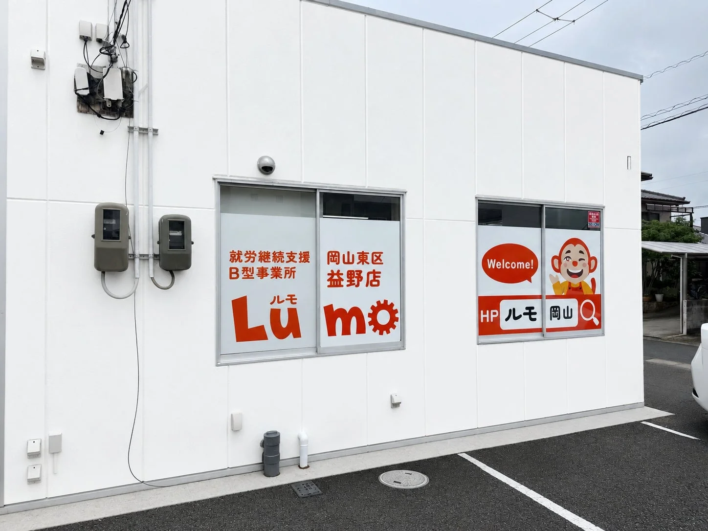 白い外壁の建物に「就労継続支援B型事業所 ルモ 岡山東区 益野店」と書かれた看板が掲げられています。