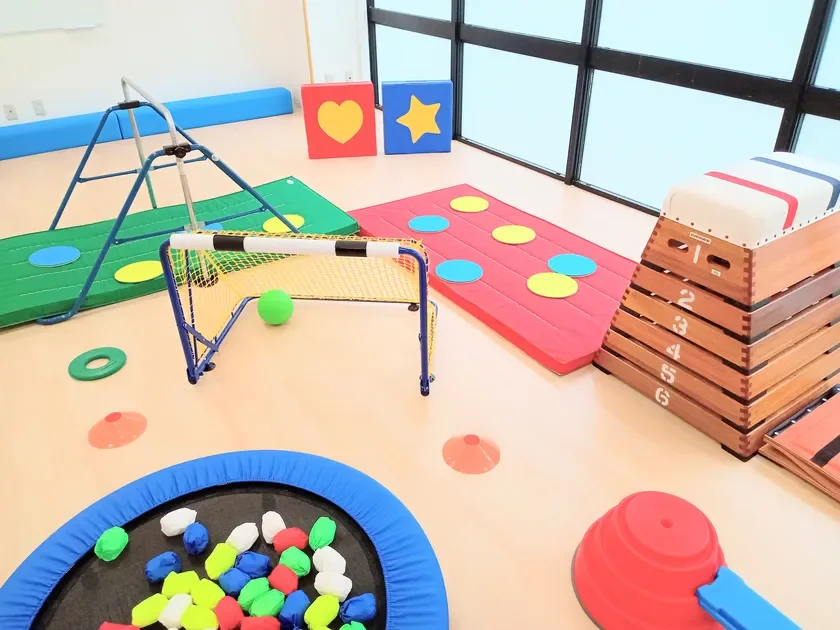 室内で様々な遊具や運動器具が配置された子供向けの遊び場。跳び箱、ミニサッカーゴール、鉄棒、トランポリン、カラフルなマットなどがあり、幼児体育や運動に適した環境。