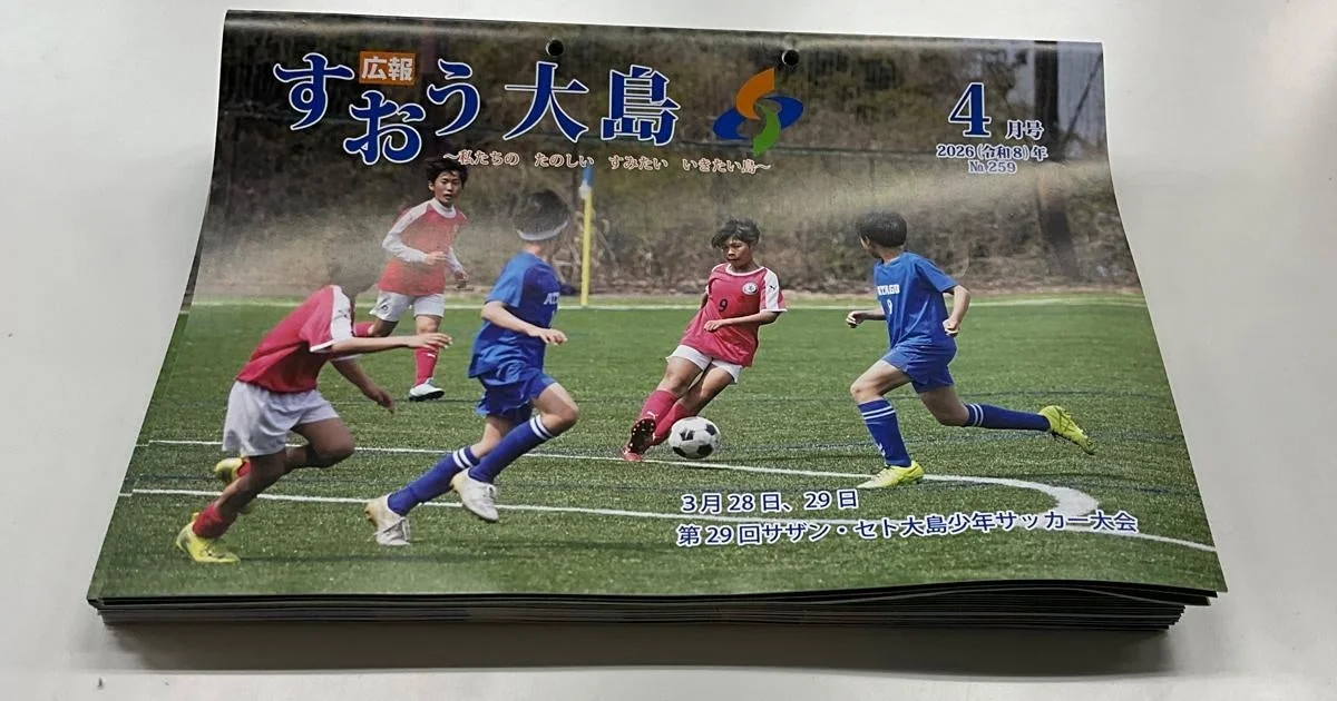 「広報すおう大島」2026年4月号の表紙で、芝生のグラウンドで少年たちがサッカーをしている様子