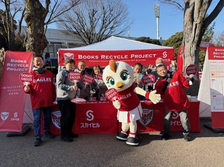横浜キヤノンイーグルスのマスコットと関係者が書籍リサイクルを呼びかける様子