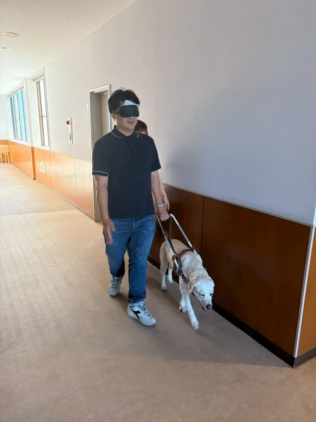 盲導犬に誘導されながら廊下を歩く男性
