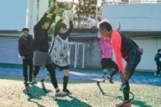 屋外のグラウンドで、数人の人々が運動している様子。一部の参加者は義足を使用している。